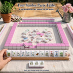 Garden mahjong game on a patio table: pink-backed tile walls, face-up tiles in the center, a rack of 13 tiles, three Jokers