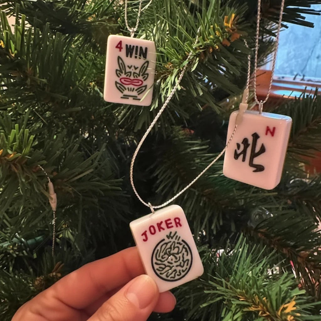 Pink mahjong tile ornaments held in front of a tree: a wind tile and a joker