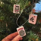 Pink mahjong tile ornaments held in front of a tree: a wind tile and a joker