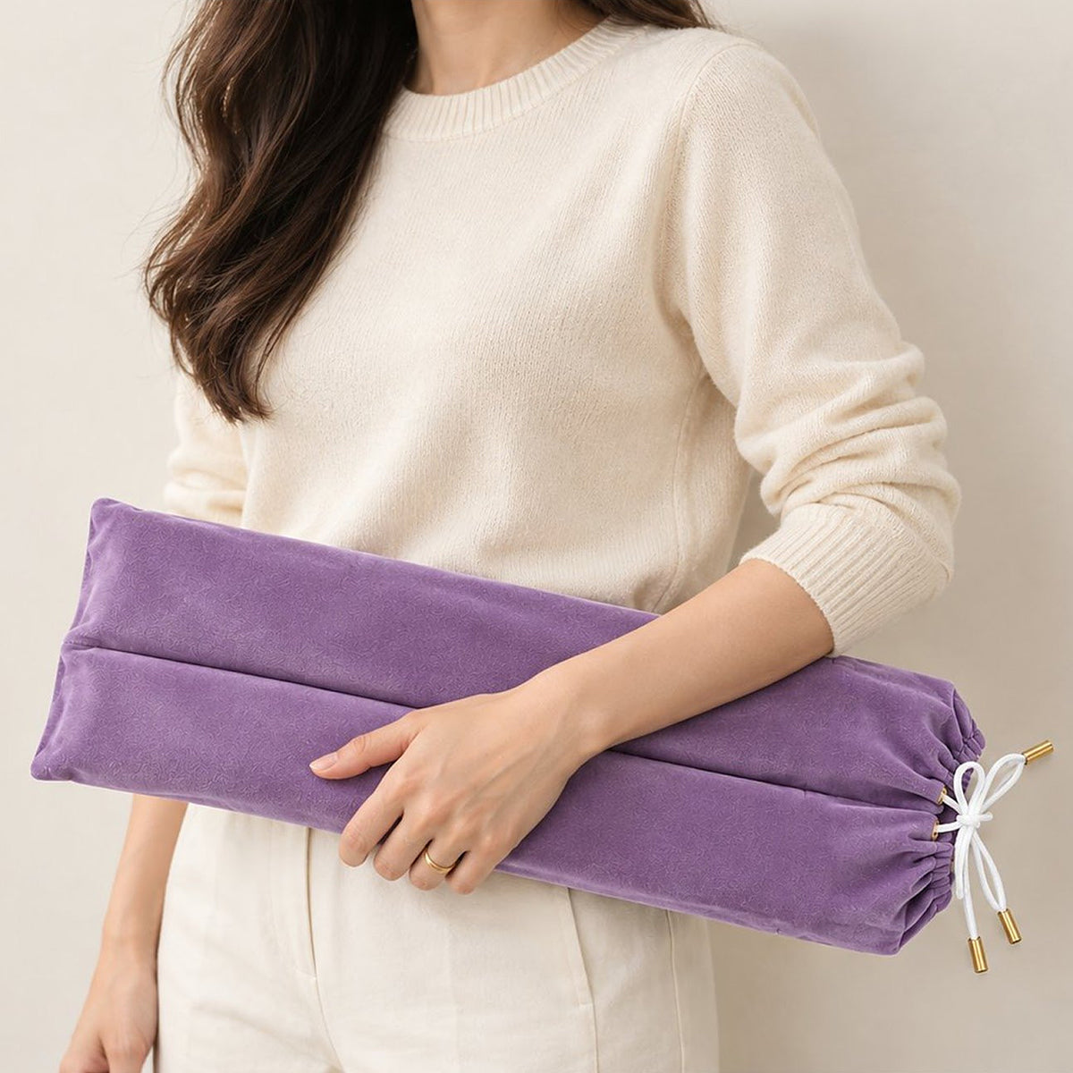 Woman in a cream sweater carrying a lavender velvet mahjong rack bag with a white drawstring bow